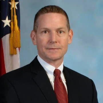 Eric Ives profile photo. Behind him, the flag of the United States of America.