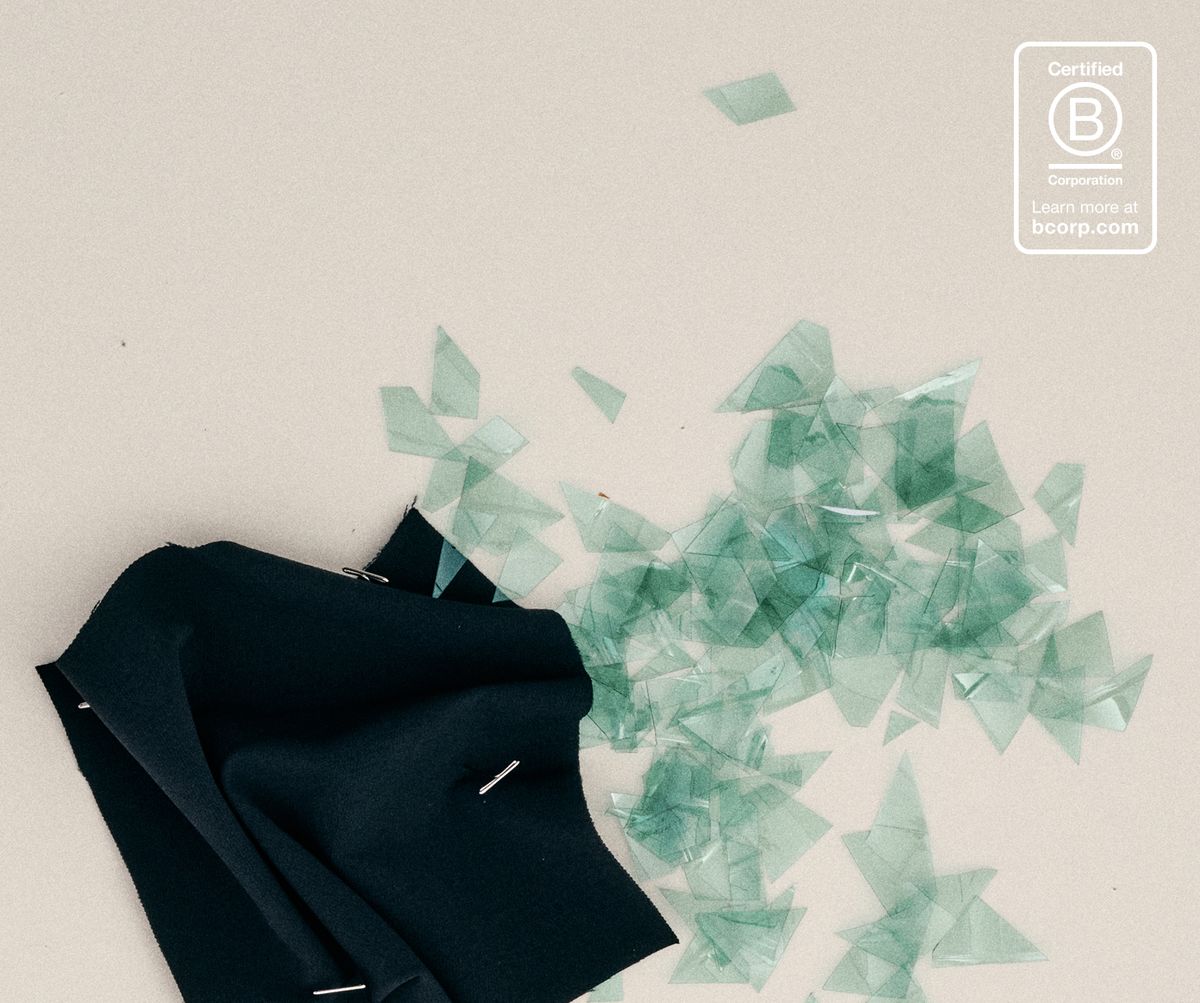Dark recycled fabric swatch beside the shredded green plastic bottle flakes it is made from, with the Certified B Corporation mark
