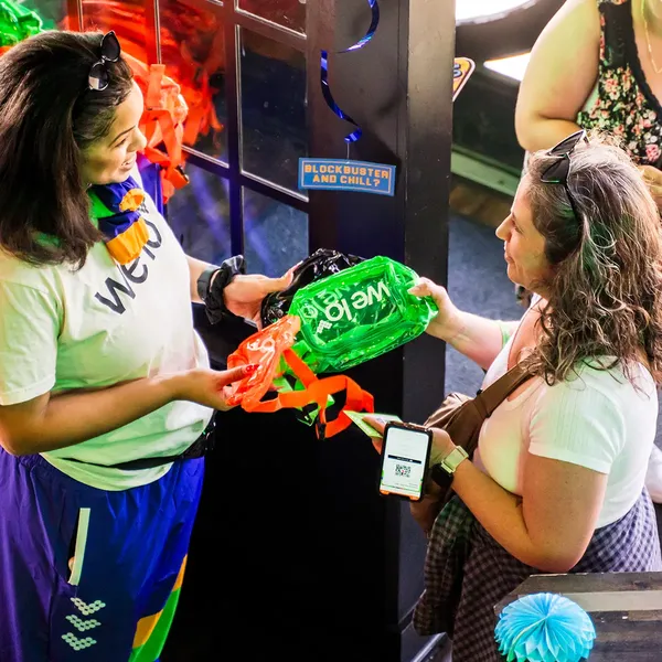 An image of a welo squad member giving away a brightly colored bag at the 90s bar takeover event at Grandview Cafe.