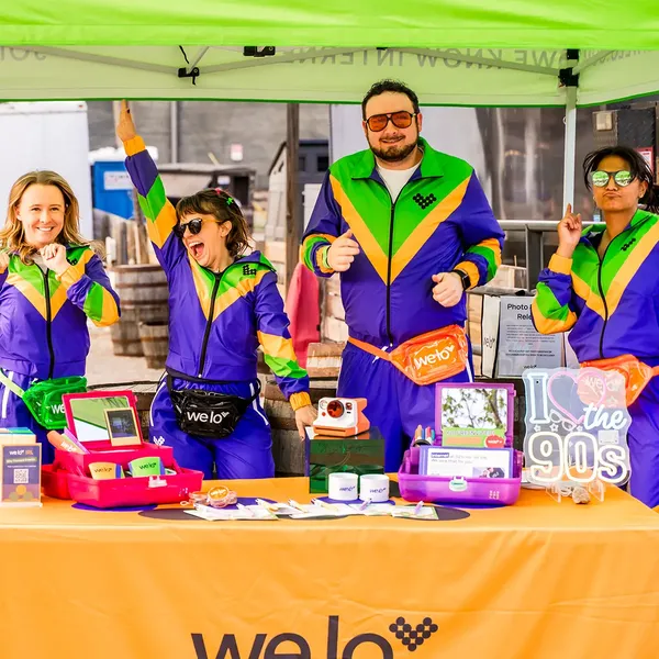 An image of 4 welo squad members in matching 90s-style purple and green tracksuits posing under a welo event tent at Land Grant.