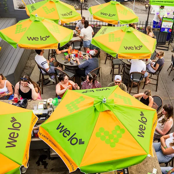 An image of the people socializing under welo-branded green and orange umbrellas at the 90s bar takeover event at Grandview Cafe.