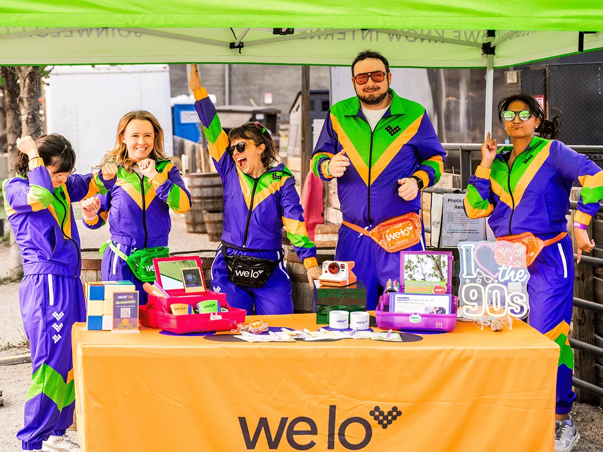 An image of 5 welo squad members in matching 90s-style purple and green tracksuits posing under a welo event tent at Land Grant.