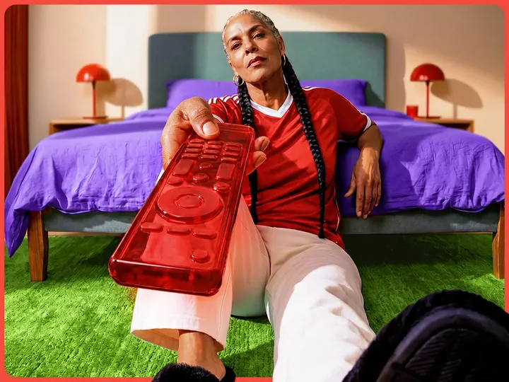 A welo customer sitting on a green rug points a transparent red remote control at the screen.