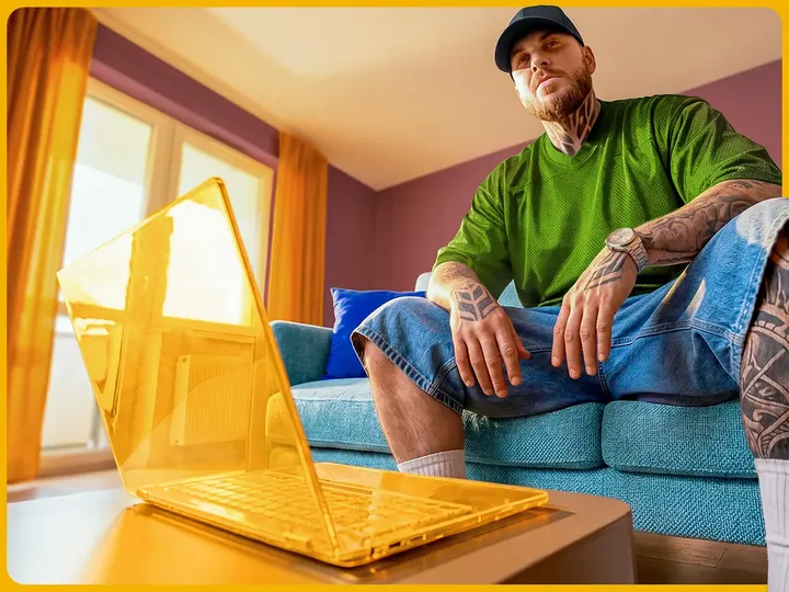 A casual customer sitting on a blue couch at home next to a bright yellow laptop.