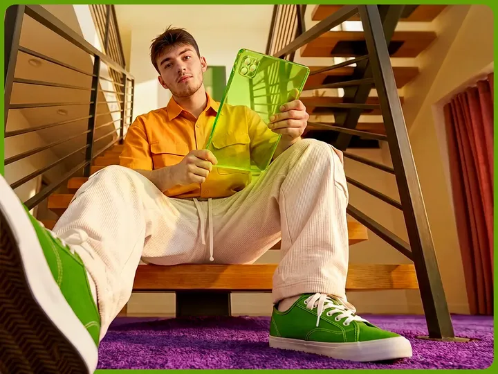 A smiling young man sits on wooden stairs holding a bright green tablet, ready to share a referral code.