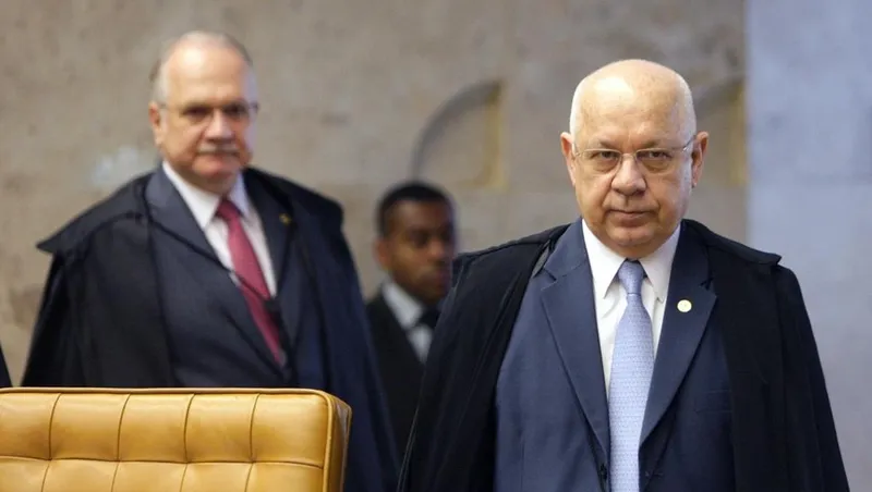 Um juiz de toga em primeiro plano, olhando para frente, com outras pessoas desfocadas ao fundo, em um ambiente de tribunal.