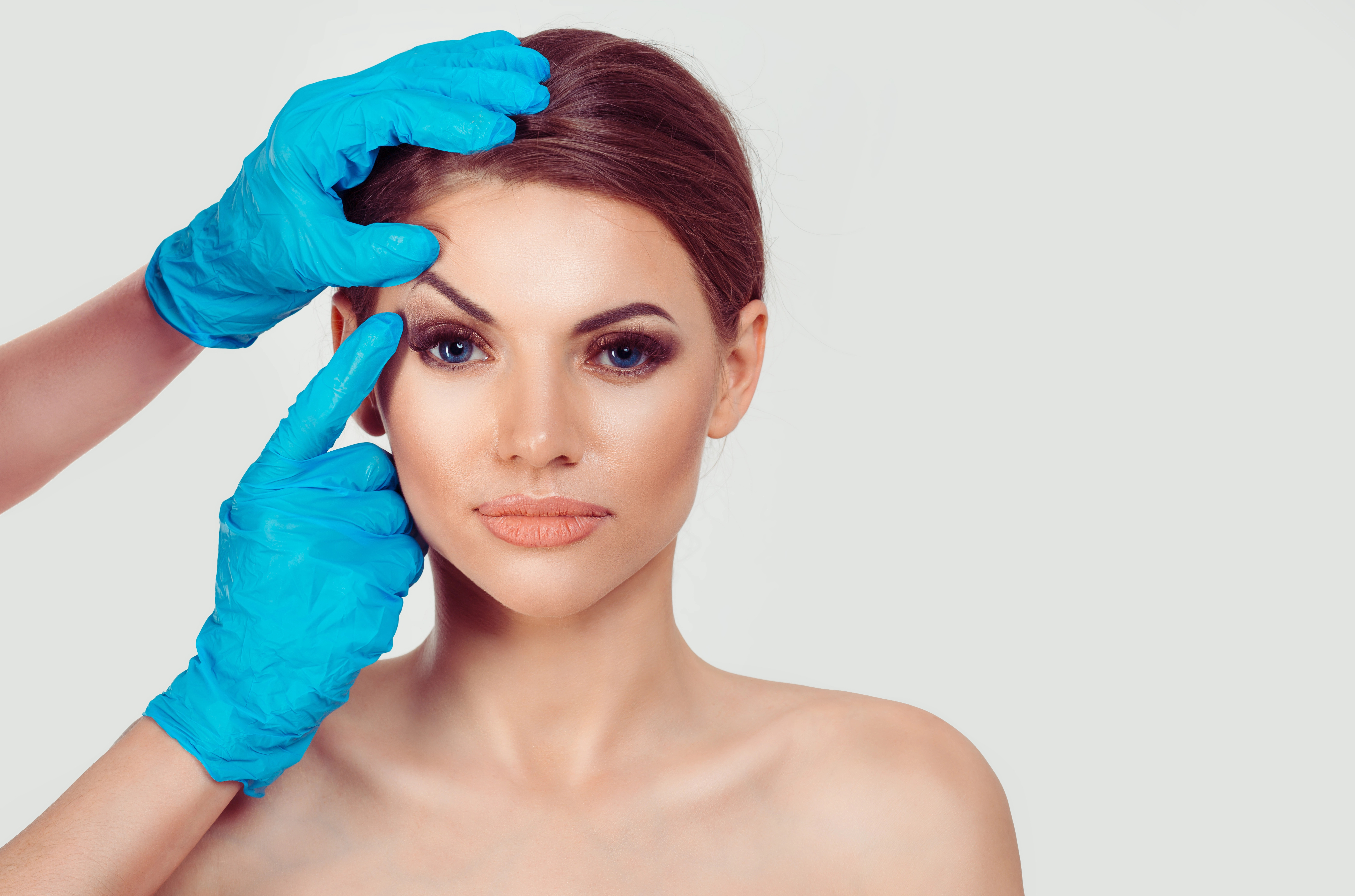 A woman with neutral expression has her face examined by gloved hands for cosmetic consultation or procedure.