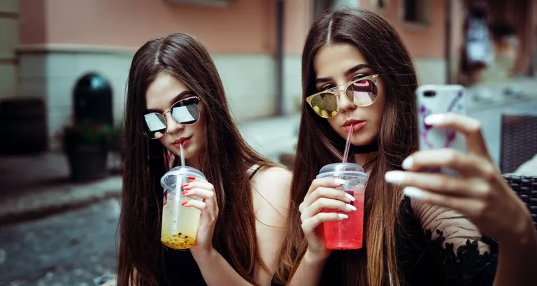 Teenage girls with drinks taking a selfie.