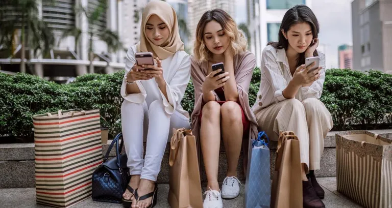 Three girls sit on their phones with shopping bags after a long day of shopping.