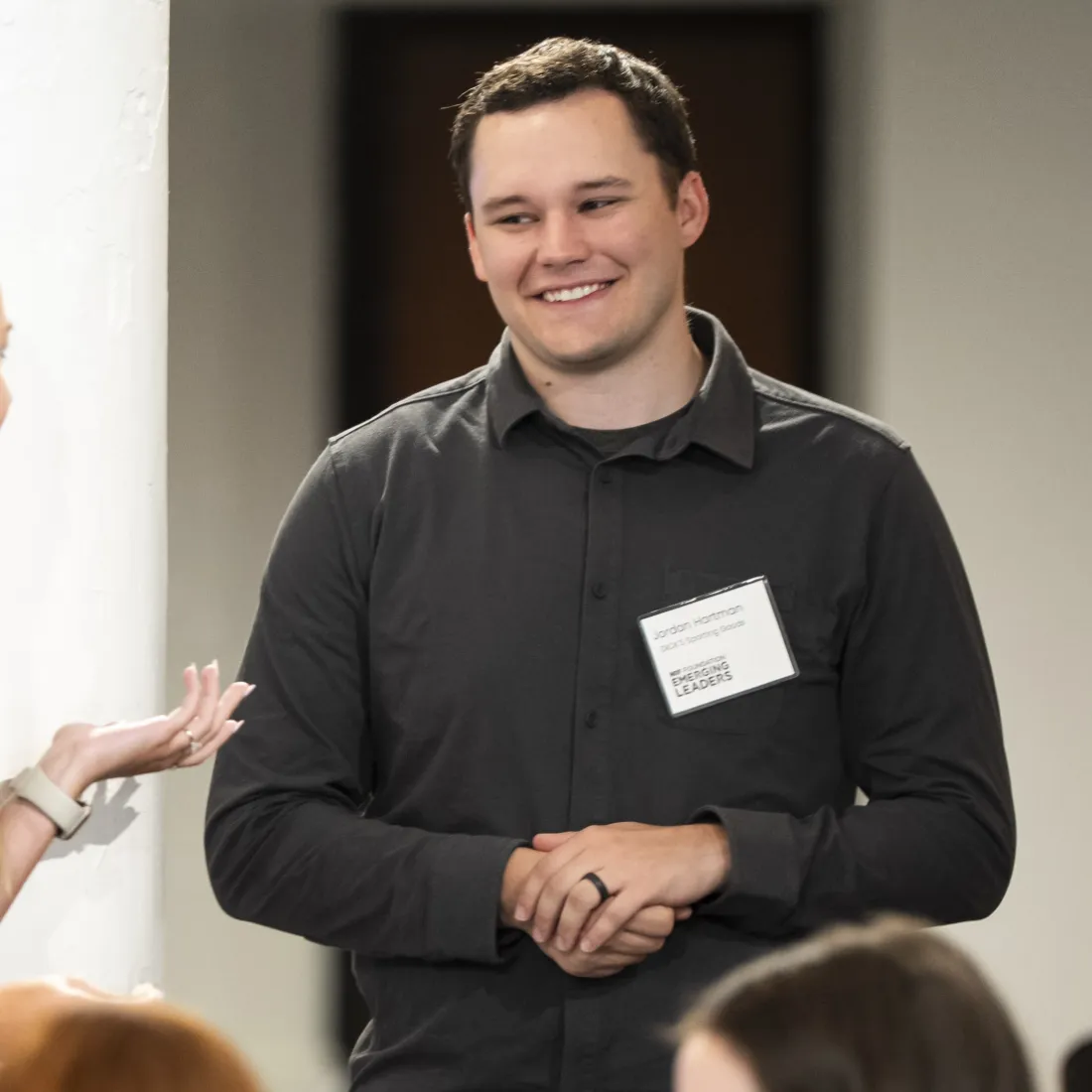 A young man in a grey shirt is smiling while he listens to a young woman during a collaborative workshop.