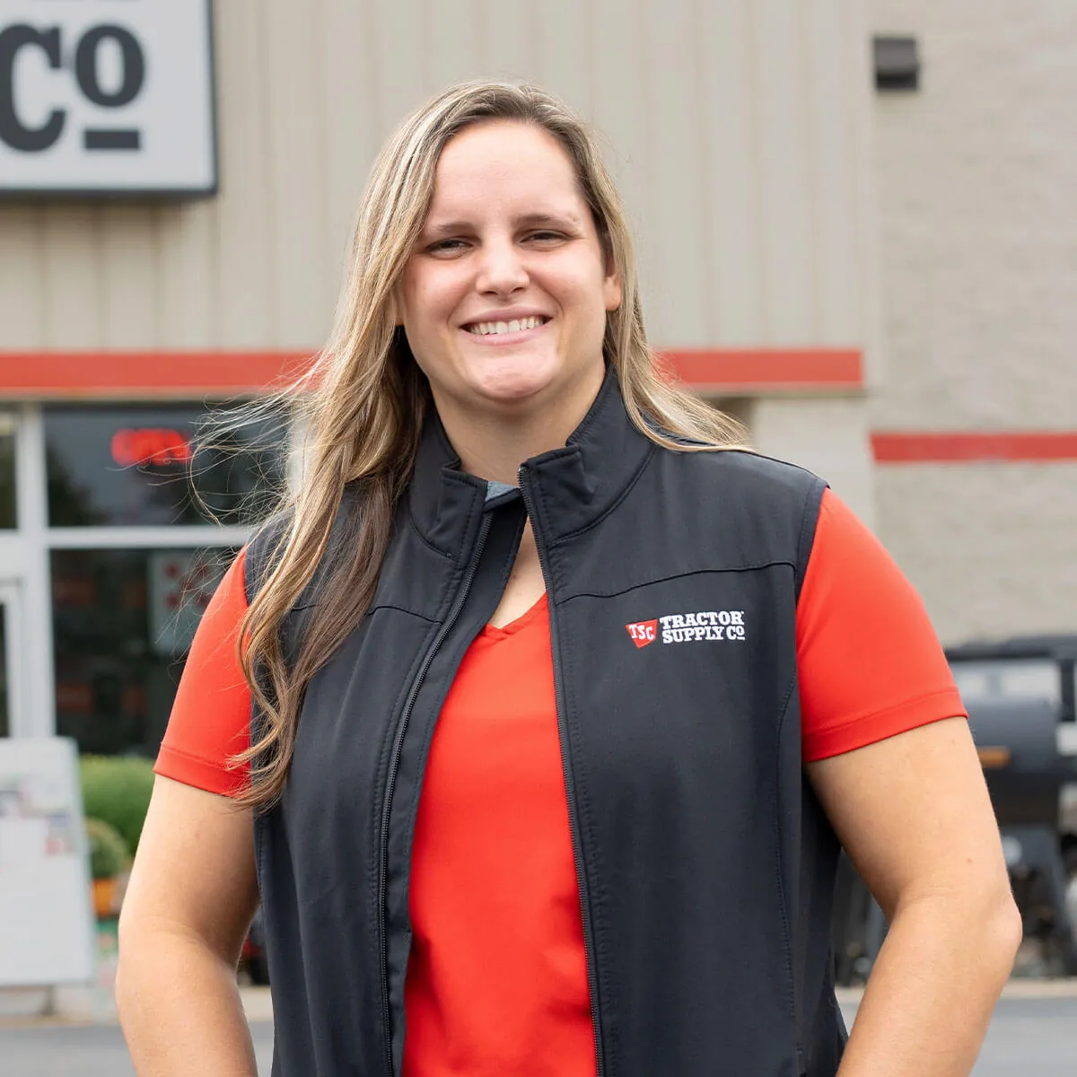 Savannah Clark wears a Tracxtor Supply Co. vest and red shirt smiles in front of her store.