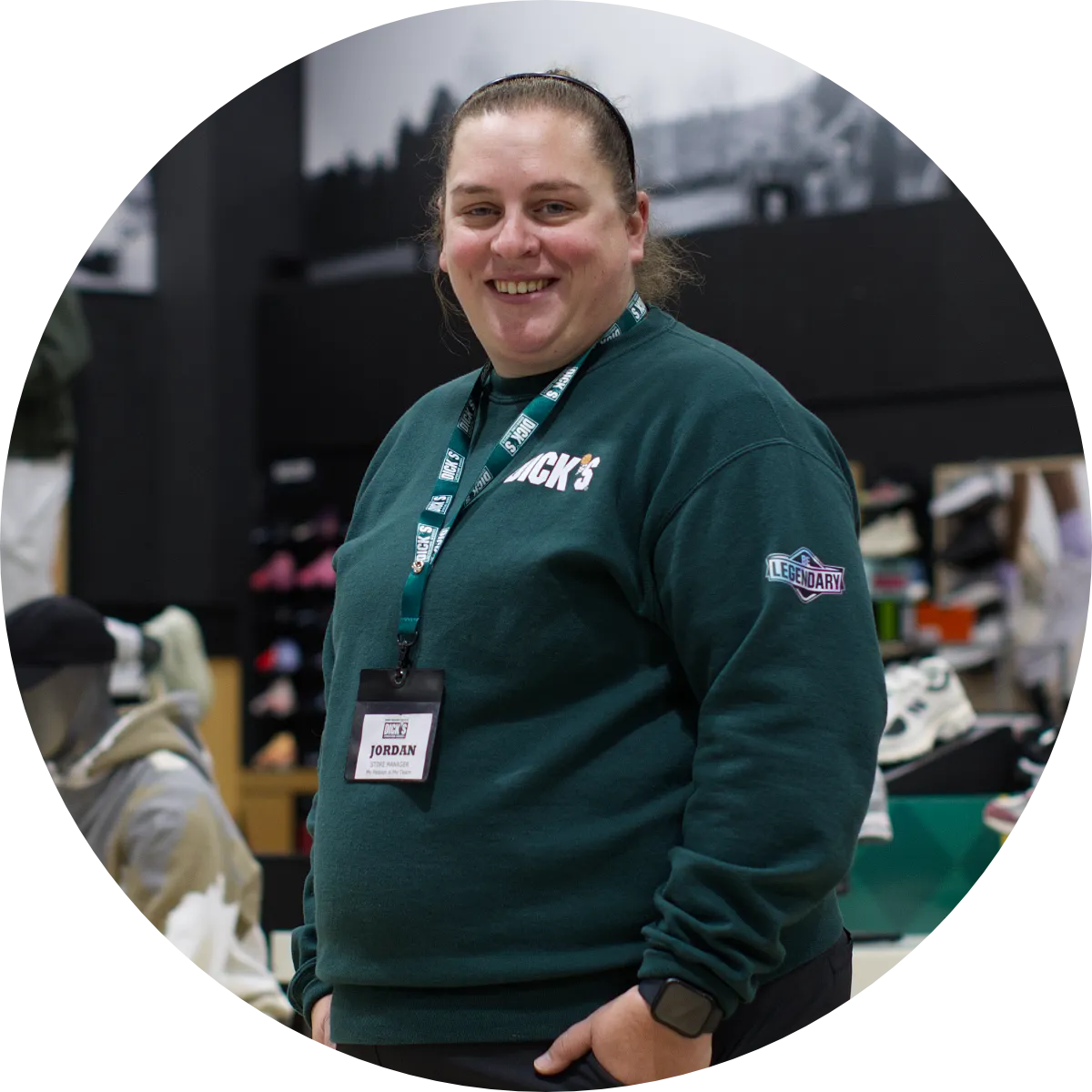 A representative of DICK'S Sporting Goods, in a green crew neck sweater, poses for the camera on the store's shopping area..