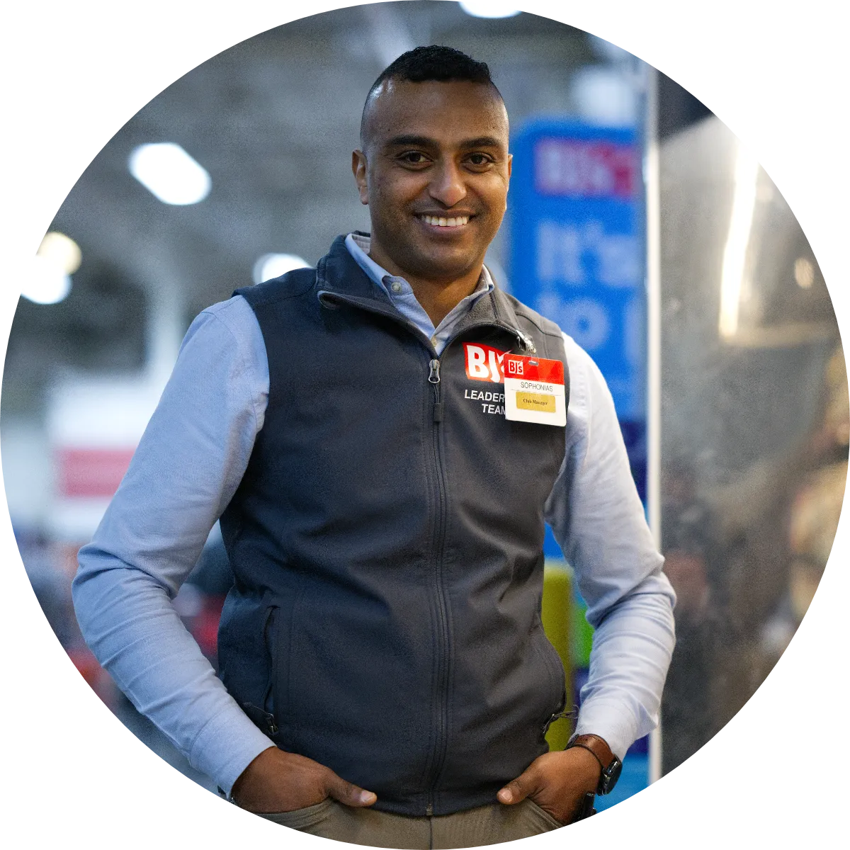 A representative from BJ's poses in a vest and blue collared shirt next to a refrigerated store display.