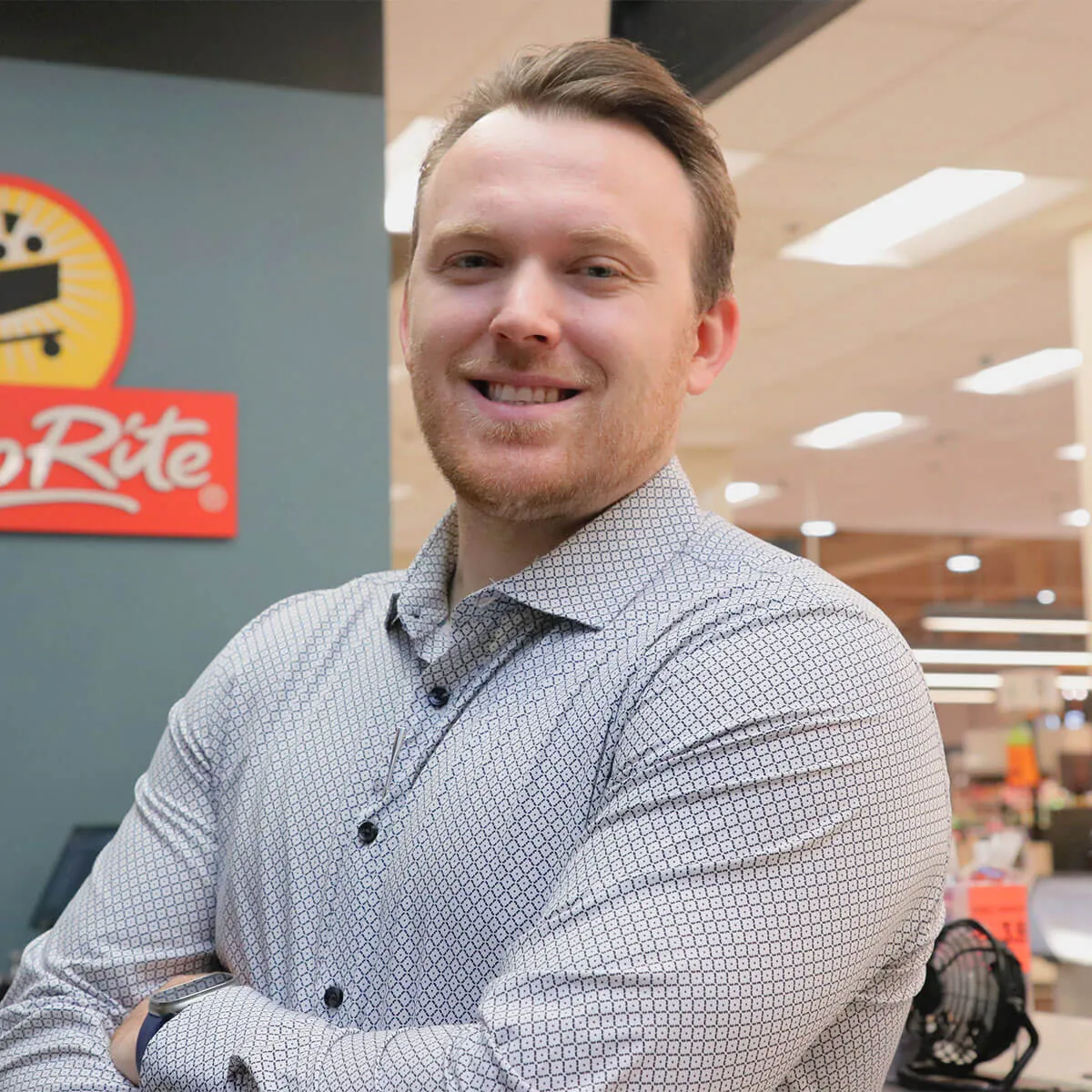 James Wallace wears a patterned shirt stands smiling with arms crossed in a store setting.