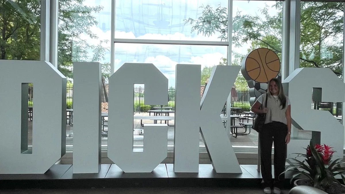 A woman stands in front of a giant, iconic series of statues spelling DICK'S at the DICK'S Sporting Goods Headquarters.