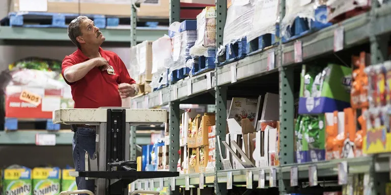 A BJ's Wholesale Club associate is using a forklift device to help manage inventory on high shelves inside the store.