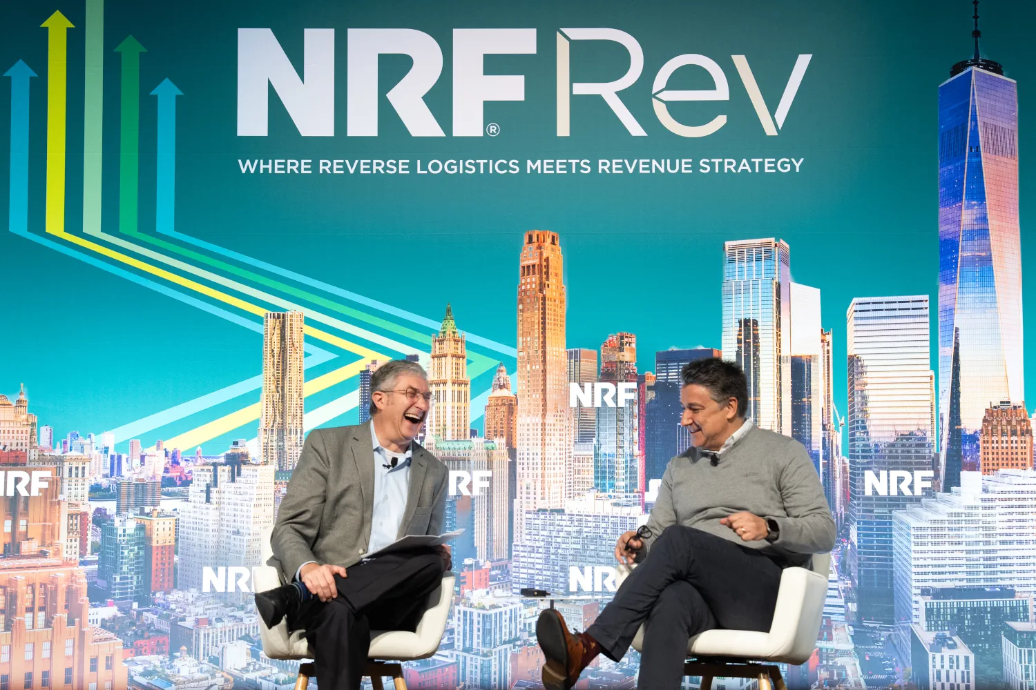 On stage and in front of a NRF Rev branded backdropm Scot Case and Javier Quiñones laugh while having a kick-off discussion NRF Rev.