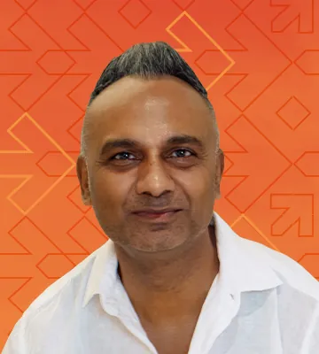 A profile photo of Dilip Patel, overlayed over an orange background with a geometric pattern of arrows and diamond shapes.
