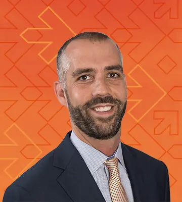 Professional portrait of Adam Lukoskie, NRF Foundation's Executive Director and National Retail Federation's Senior Vice President. The photo's background has a gradient of orange and red colors along with arrows pointing right, consistent with the NRF Foundation Student Program branding.