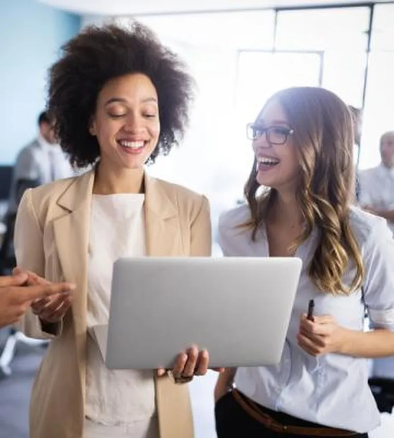 Women standing next to each other holding a laptop.