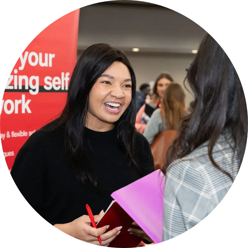 A representative from Macy's talks to a long haired person at a career fair about job prospects and internships available at Macy's Inc. Behind the recruiter is a sign with a Macy's Inc logo and the words: Bring your amazing self to work.