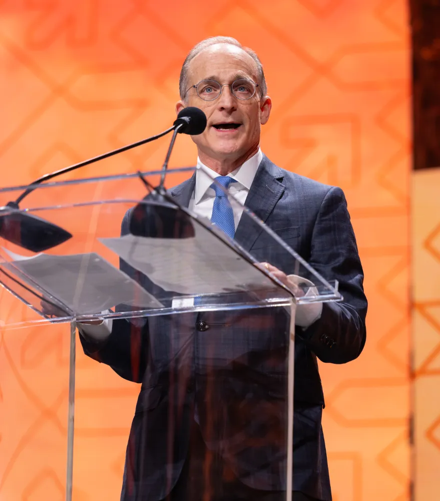 Steve Preston, board chair of the NRF Foundation, speaking at a podium with a microphone in front of an orange background.