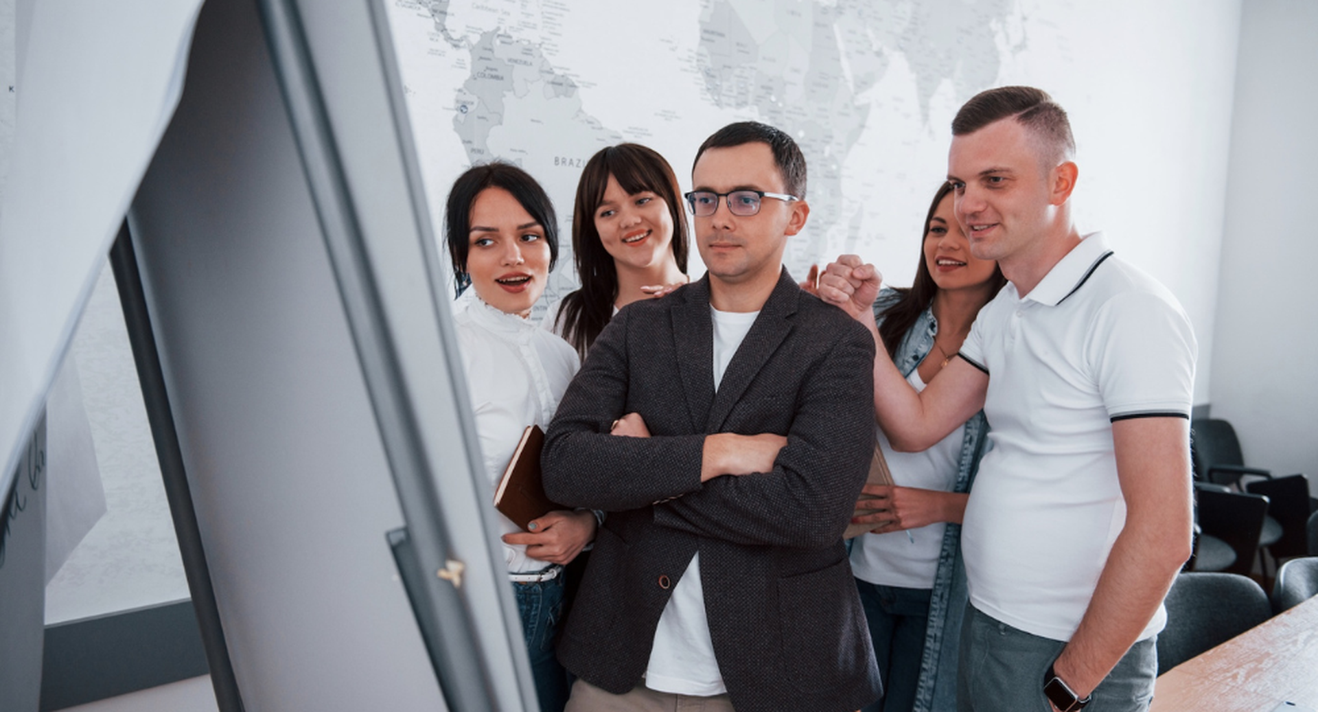 A group of five people in a meeting, gathered around a screen with a map in the background, focused and engaged.