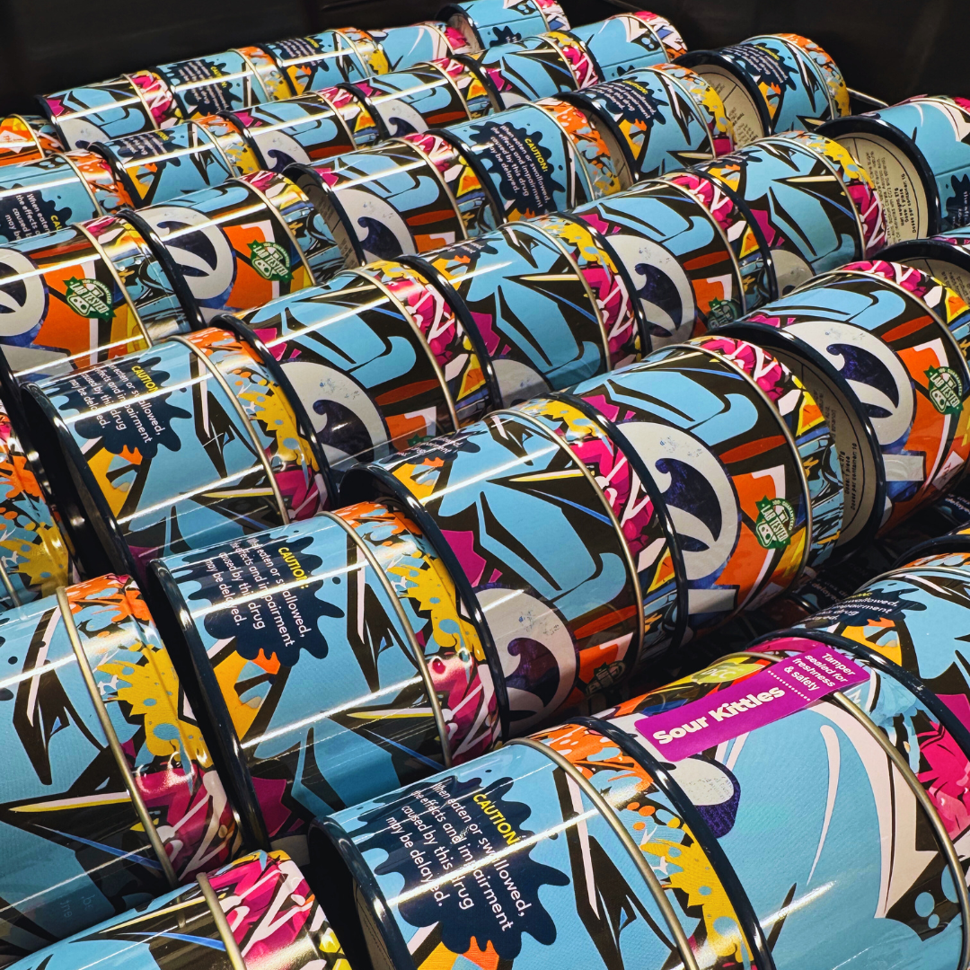 Rows of colorful, patterned tins with abstract designs, labeled "Sour Kicks," arranged neatly on a shelf.
