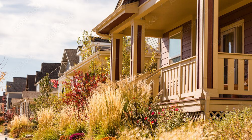 A row of colorful suburban houses with well-maintained gardens and autumn foliage along a sunny sidewalk.