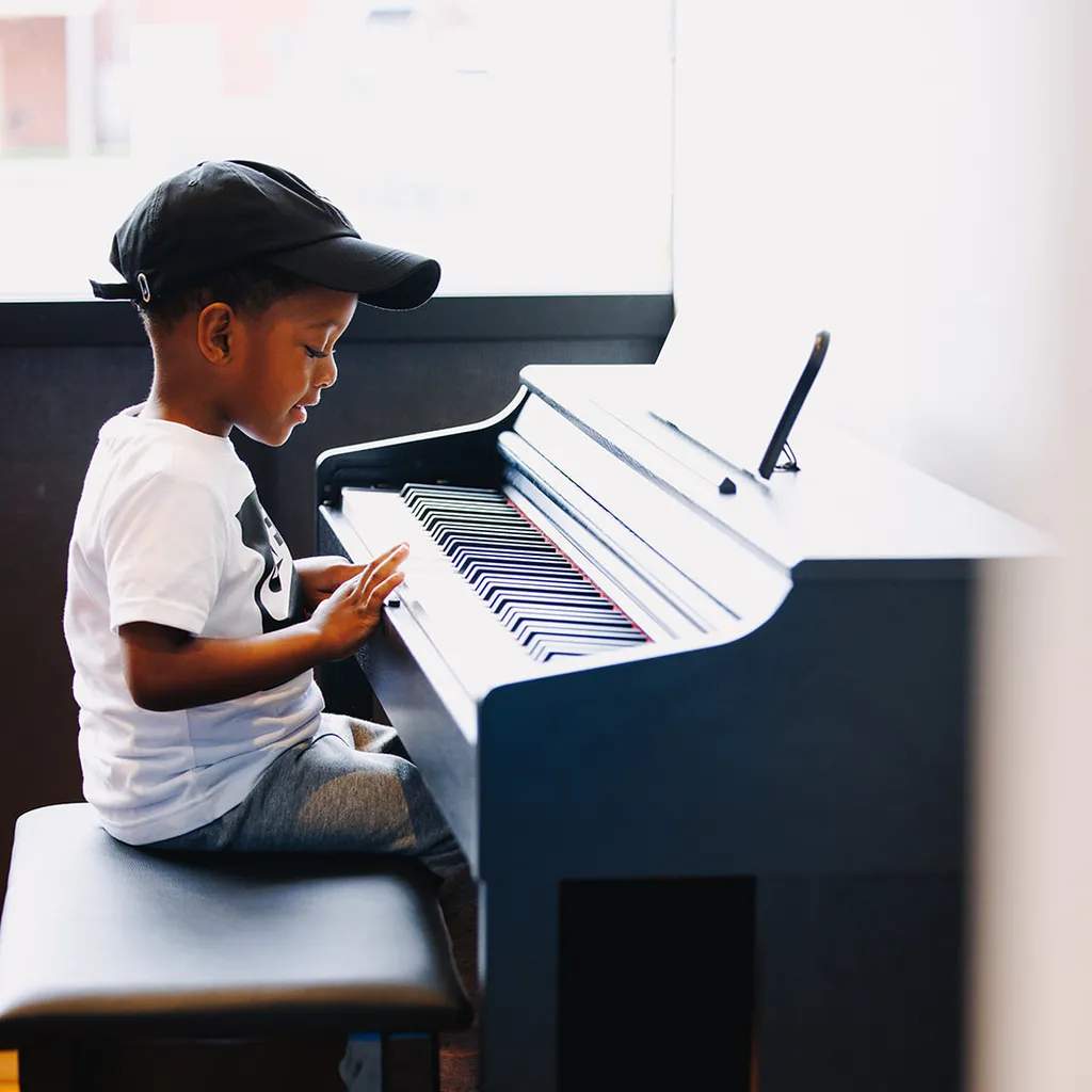 A young boy is in his own world, seated at a piano and exploring its sounds