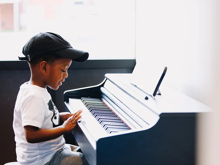 A young boy is in his own world, seated at a piano and exploring its sounds