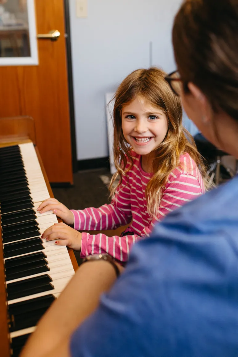 Girl sitting at a piano smiling at her teacher