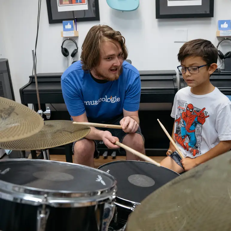 Boy sitting at the drums in a lesson with his teacher