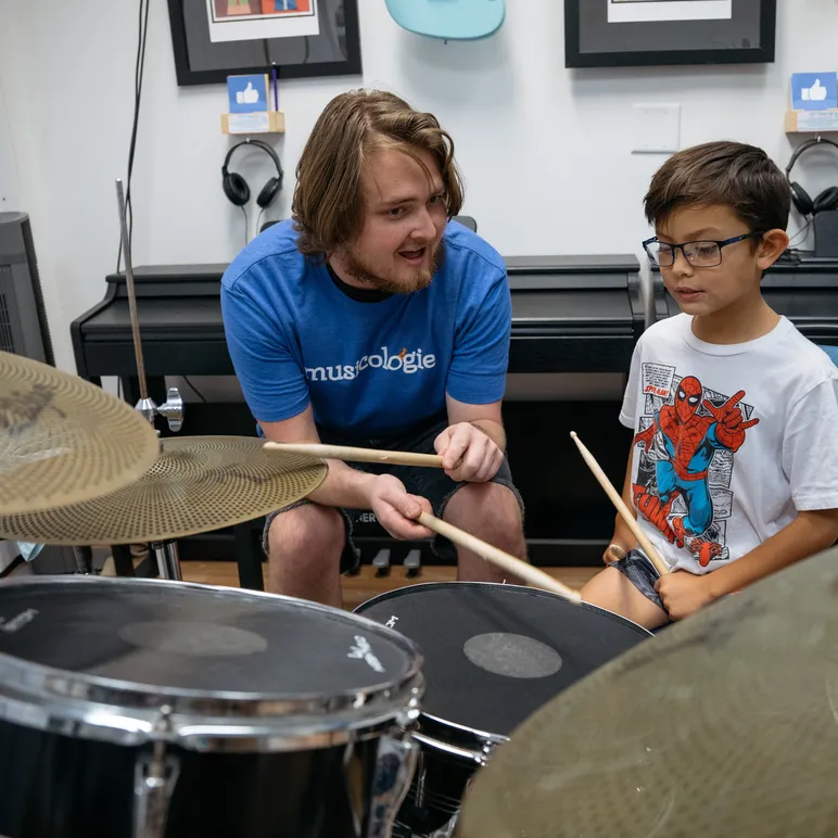Boy sitting at the drums in a lesson with his teacher