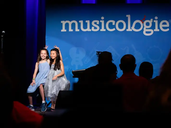 Two Girls On Stage Smiling and Giving Each Other Bunny Ears