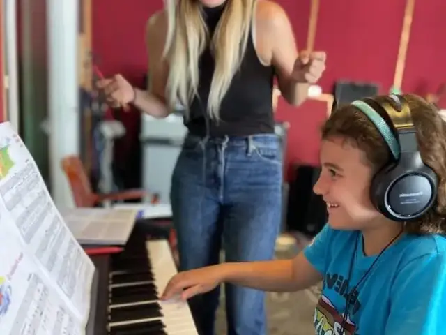 Accelerated Piano Lab student playing piano while their teacher smiles