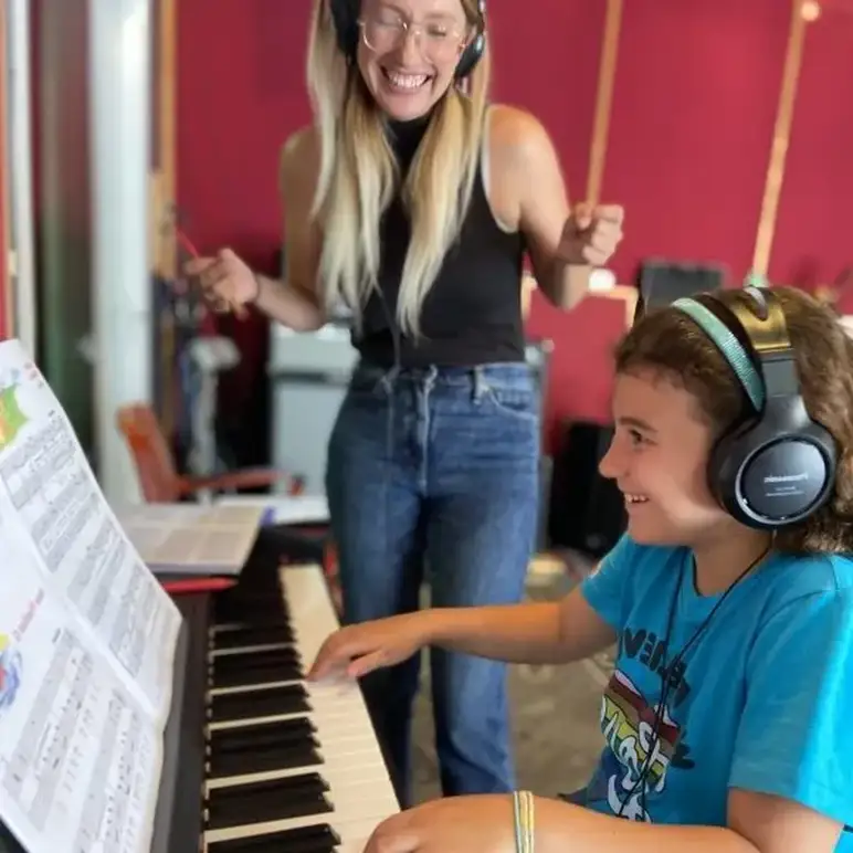 Accelerated Piano Lab student playing piano while their teacher smiles