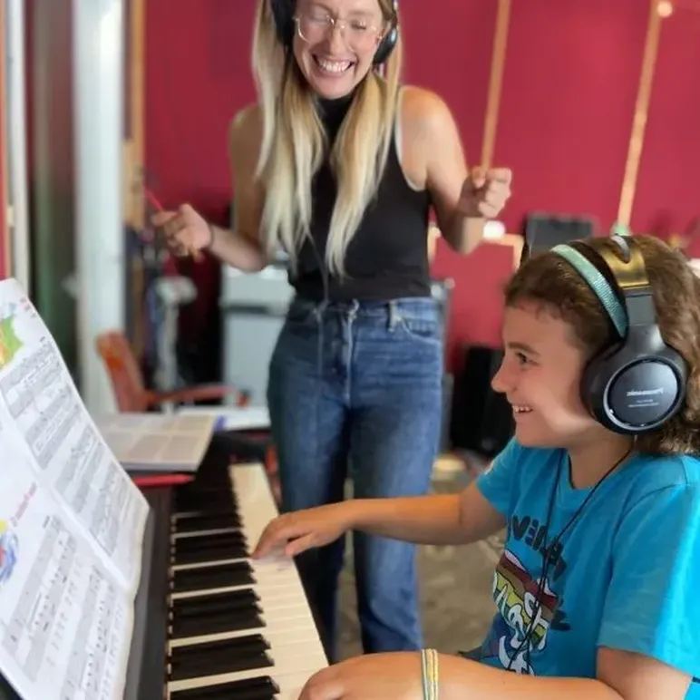 Accelerated Piano Lab student playing piano while their teacher smiles