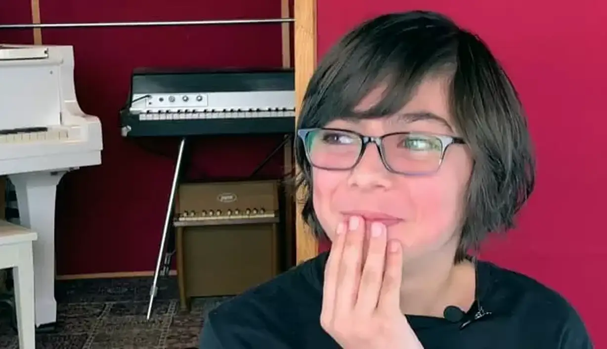 A young boy with his hand on his face, thinking about how Musicologie has impacted his life, getting ready to share his experience.