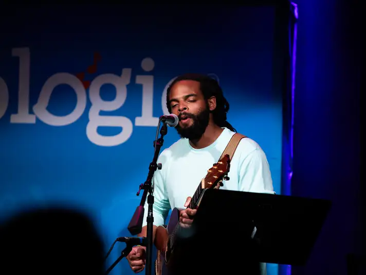 Man Playing Acoustic Guitar and Signing into a Microphone on Stage
