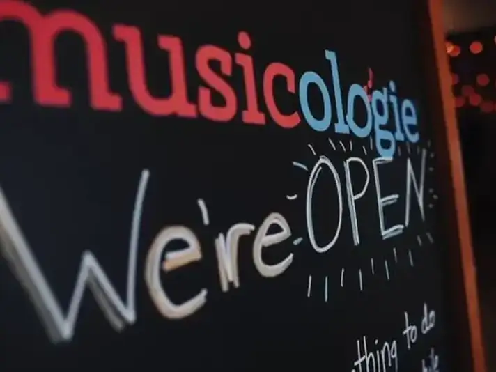 A welcoming Musicologie sandwich board that says "We're open!"