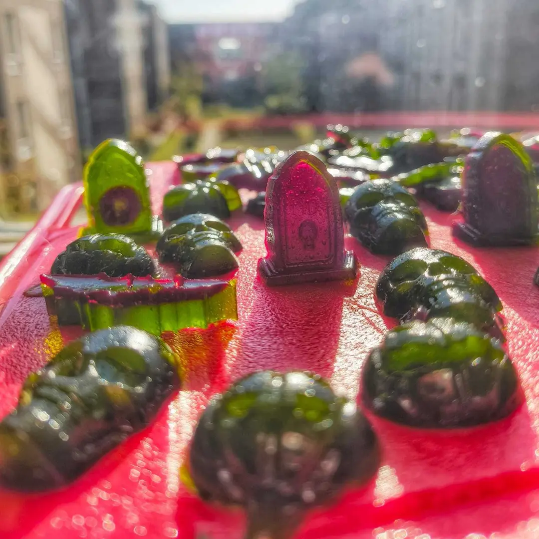 Gummy candies shaped like skulls and tombstones on a red surface, with a blurred outdoor cityscape in the background.