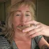 Person with blonde hair eating a slice of bread, wearing a striped shirt, with a tattoo on their finger, in an indoor setting.
