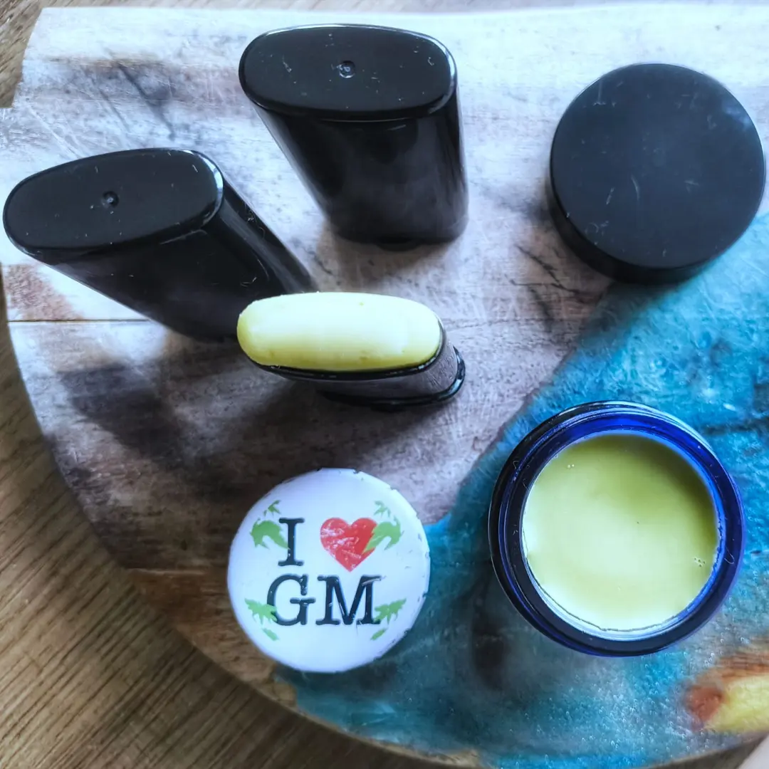 Overhead shot of black deodorant sticks, an exposed yellow stick, an open blue jar of balm, and a white