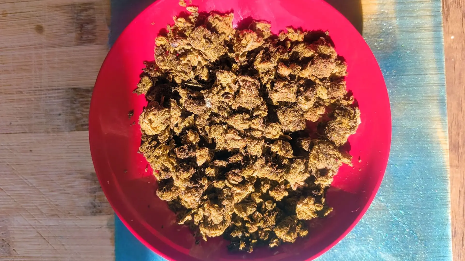 A red bowl filled with a large quantity of crumbled, brownish-green dried herbs or plant material, placed on a wooden surface.