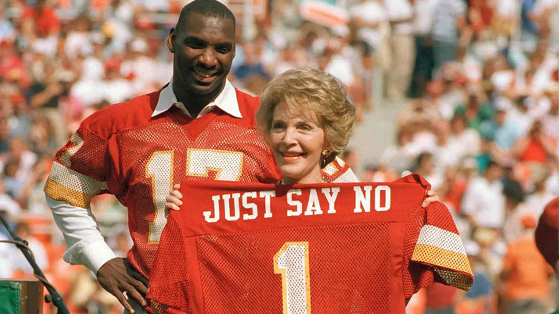Two people in red sports jerseys hold up a jersey with