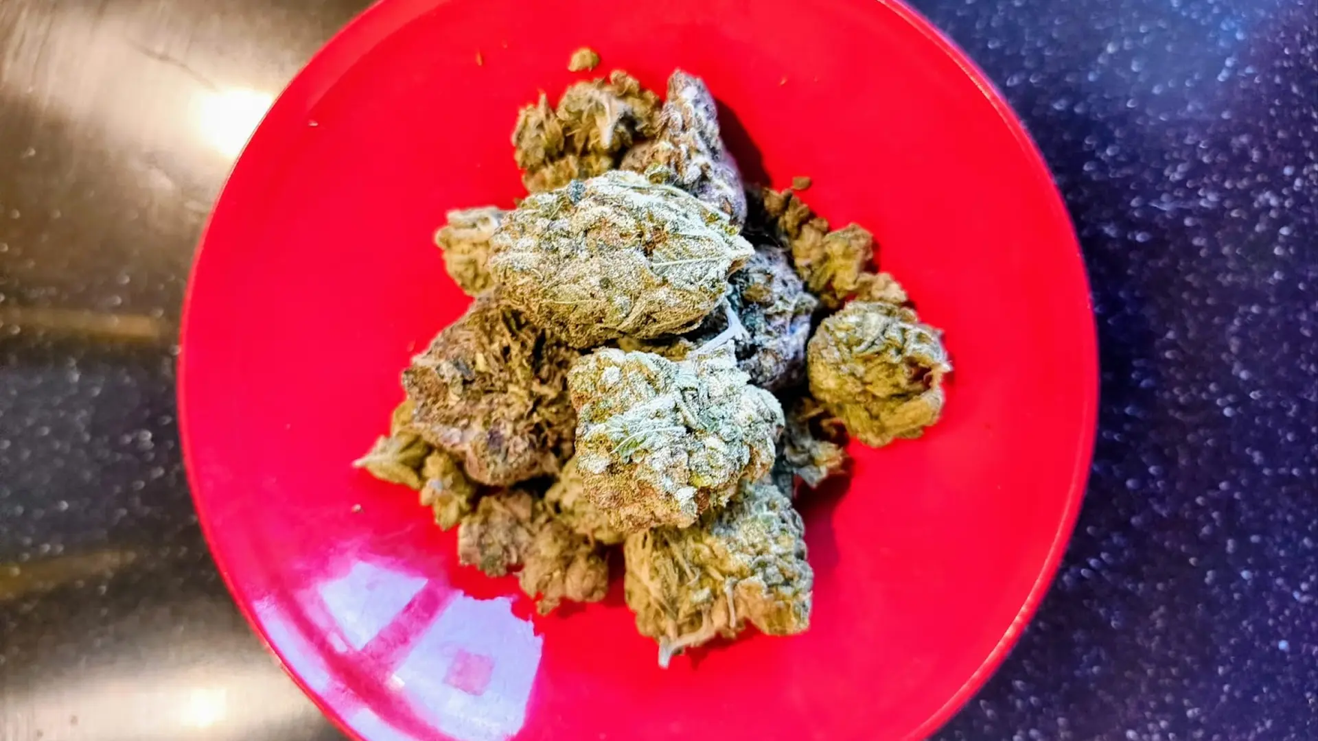 A pile of dried green herbs on a red plate, placed on a dark countertop.