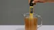 Hand holding a digital pH meter in a glass pitcher filled with brown liquid, displaying a pH reading of 6.13.