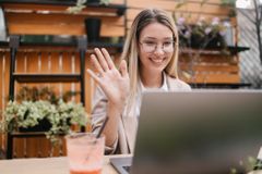 Person on laptop in outdoor coffee shop waving to screen