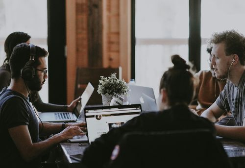 team working on laptops around table with headphones on
